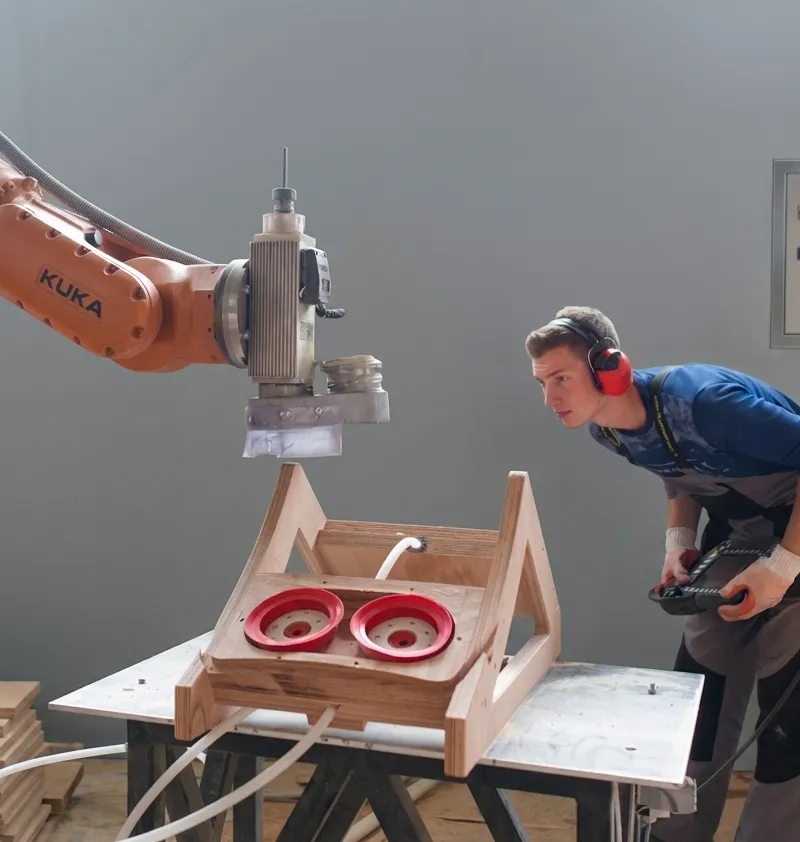 A KUKA robot arm assisting an operator on a moulding fixture.